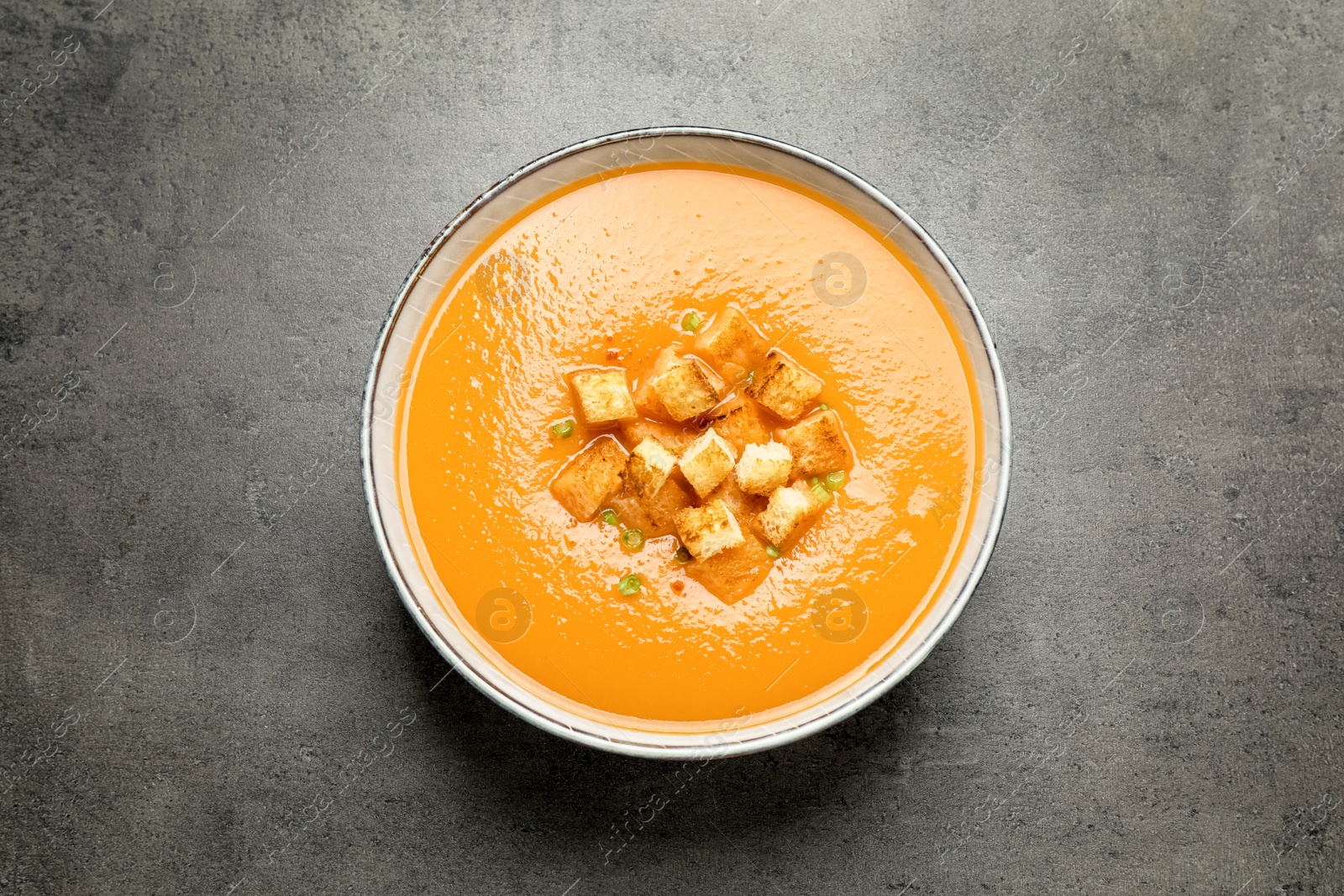 Photo of Tasty creamy pumpkin soup with croutons in bowl on grey table, top view