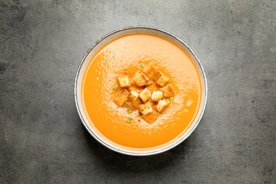 Photo of Tasty creamy pumpkin soup with croutons in bowl on grey table, top view