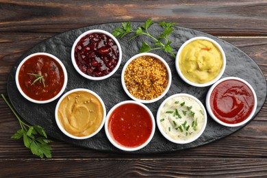 Photo of Different tasty sauces in bowls and parsley on wooden table, top view