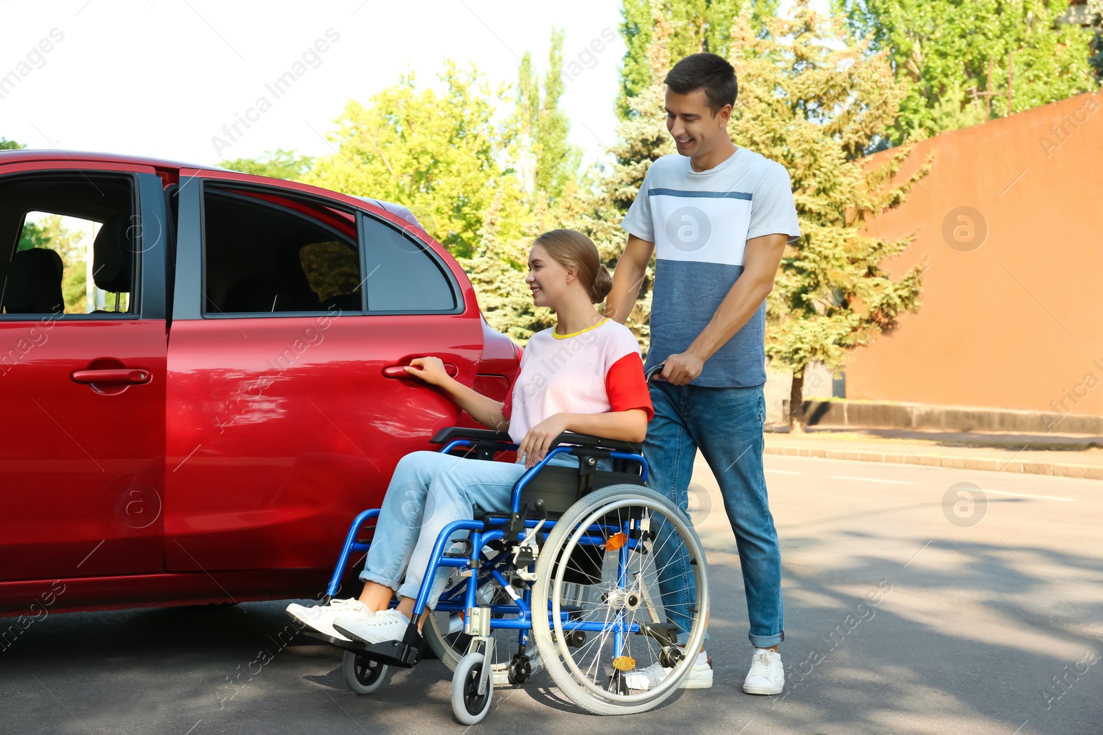 Photo of Young man helping disabled woman in wheelchair to get into car outdoors