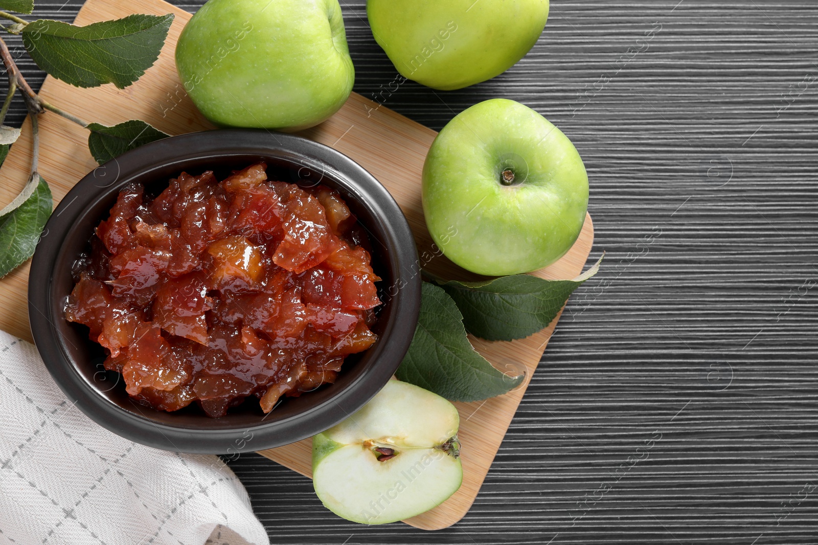 Photo of Bowl of delicious apple jam and fresh fruits on black wooden table, flat lay. Space for text