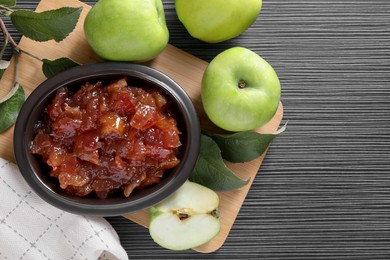 Photo of Bowl of delicious apple jam and fresh fruits on black wooden table, flat lay. Space for text