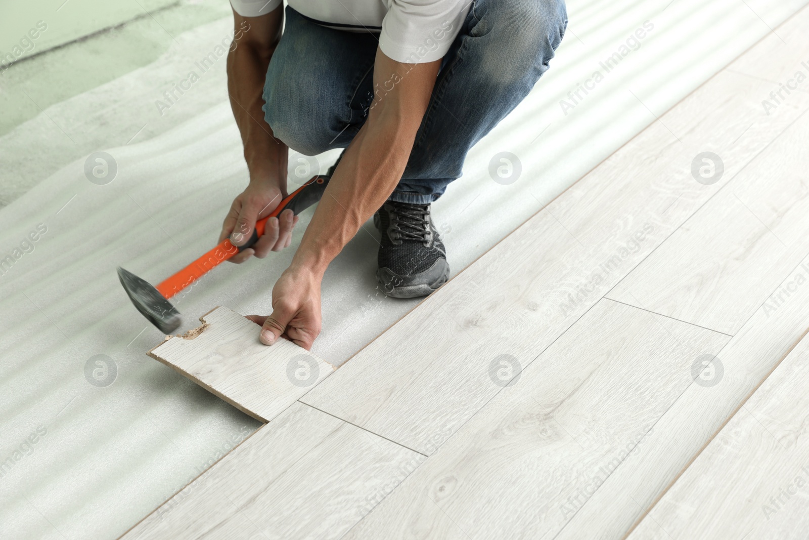 Photo of Man using hammer during installation of new laminate flooring, closeup