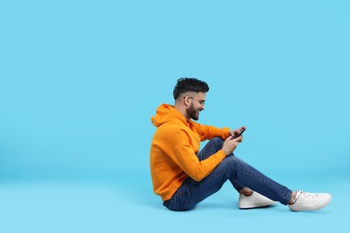 Photo of Happy young man using smartphone on light blue background, space for text