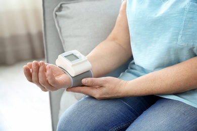 Photo of Mature woman checking pulse with medical device at home, closeup