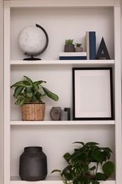Photo of Interior design. Shelves with stylish accessories, potted plants and frame near white wall
