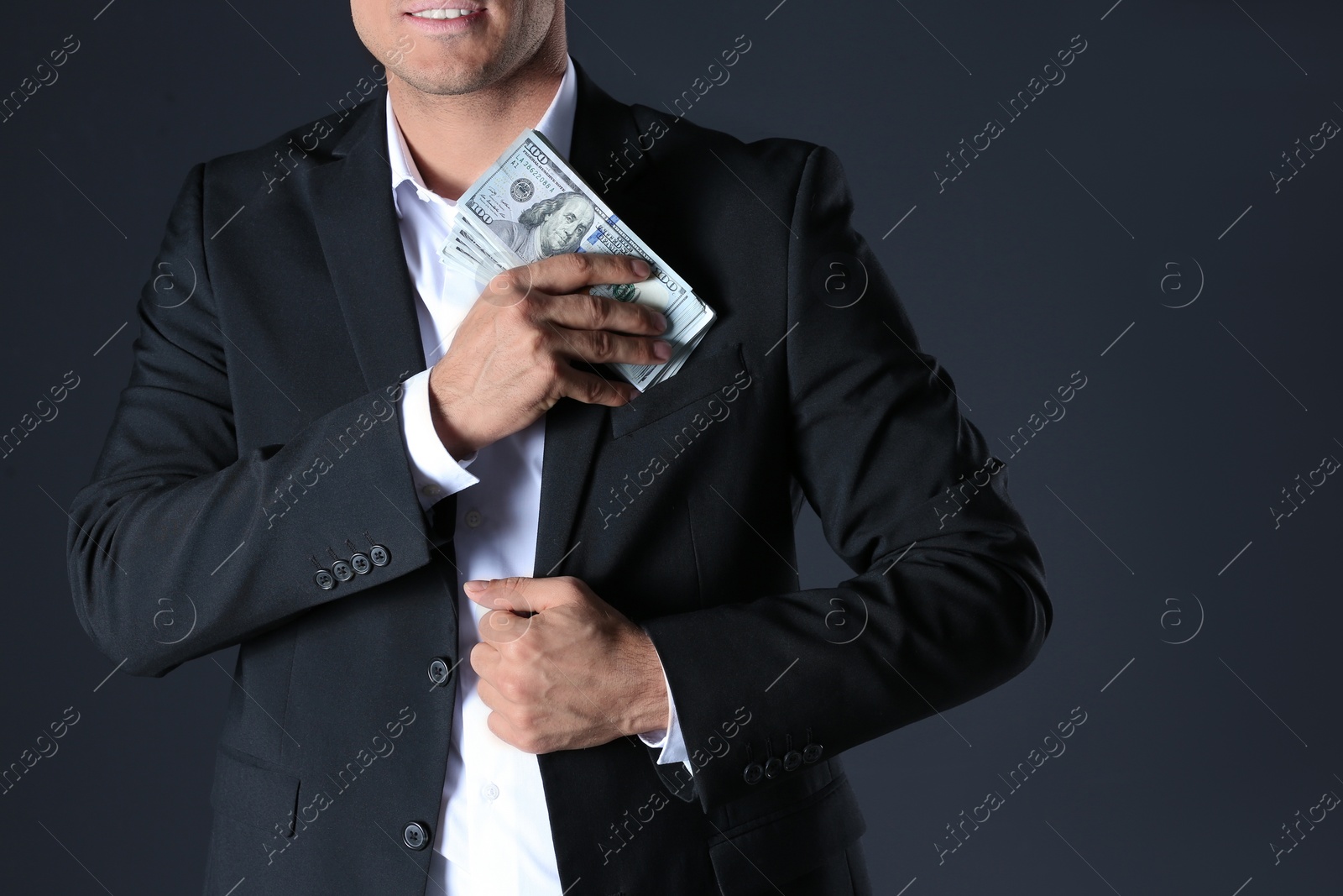 Photo of Man putting bribe money into pocket on black background, closeup