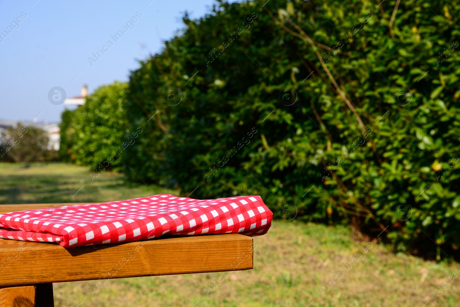 Photo of Folded red and white checkered tablecloth on wooden picnic table in park