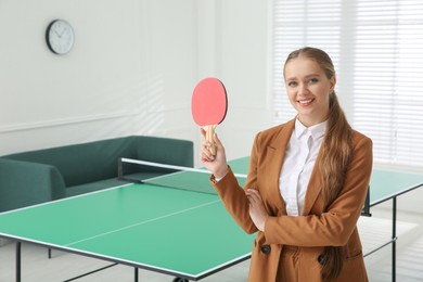 Business woman with tennis racket near ping pong table in office. Space for text
