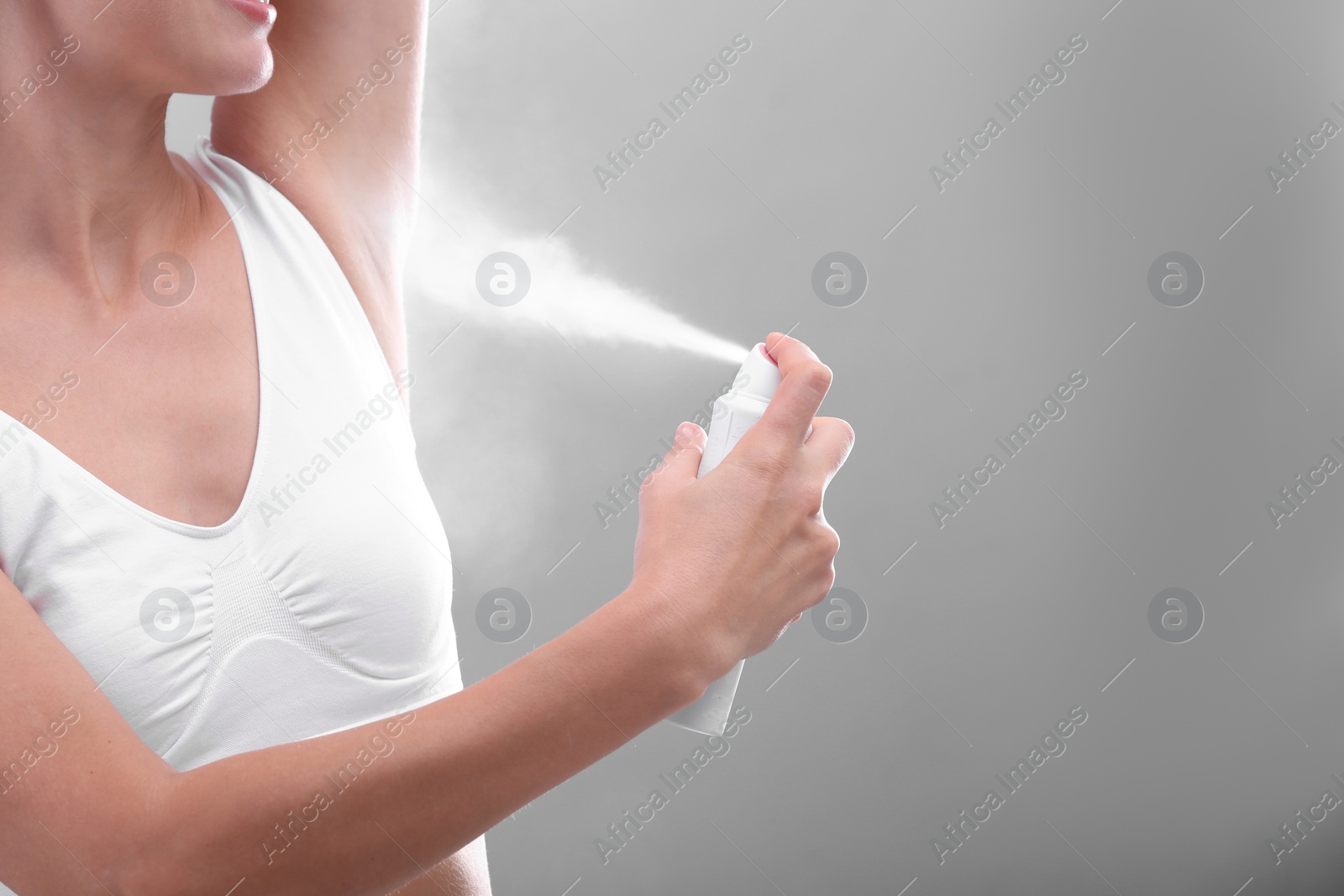 Photo of Young woman using deodorant on grey background, closeup. Space for text