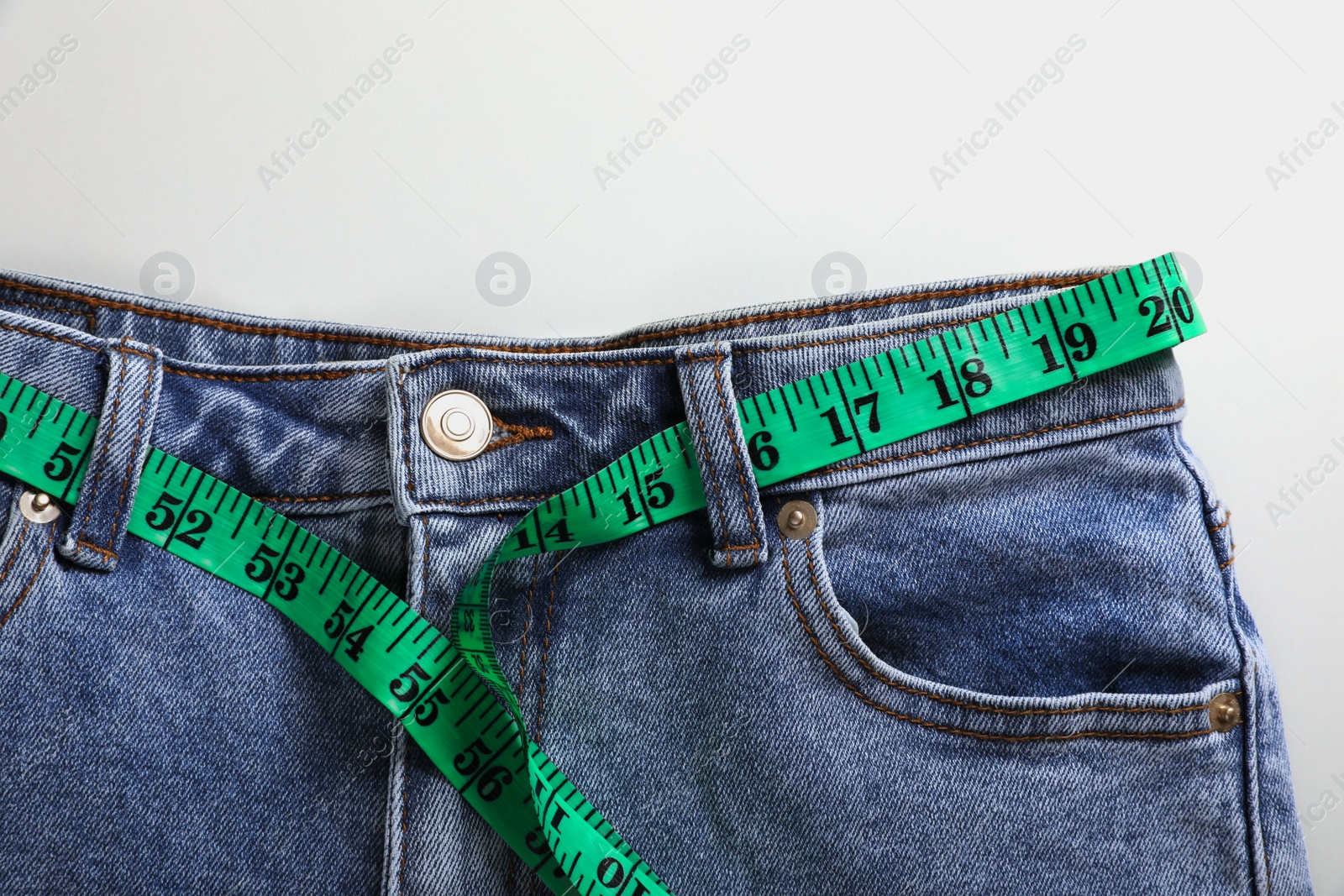 Photo of Jeans with measuring tape on light grey background, top view. Weight loss concept