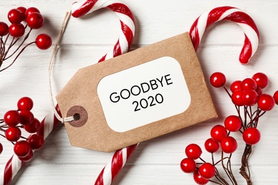 Photo of Flat lay composition with phrase Goodbye 2020, candy canes and red berries on white wooden table