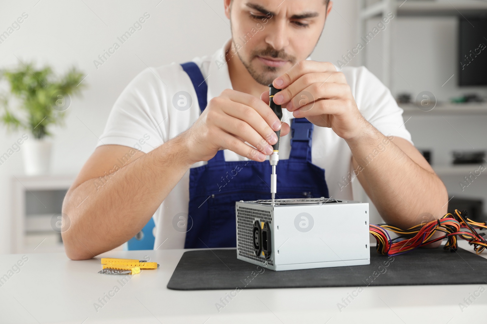 Photo of Male technician repairing power supply unit at table indoors