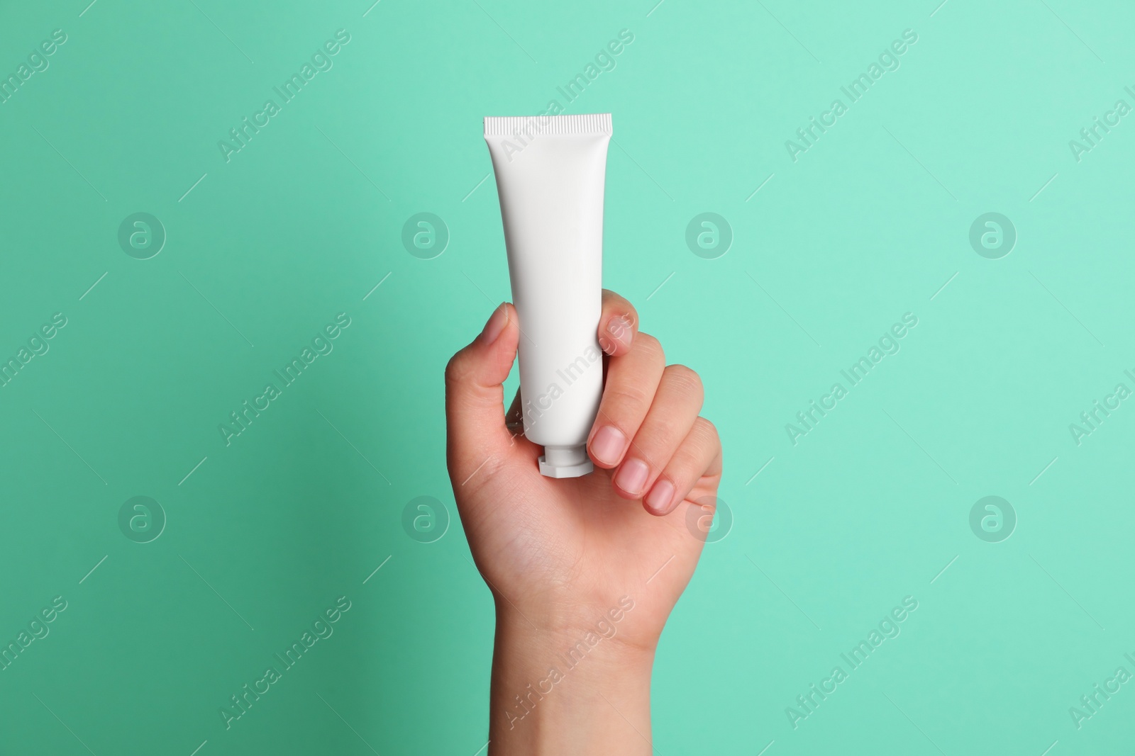 Photo of Woman holding tube of face cream on turquoise background, closeup