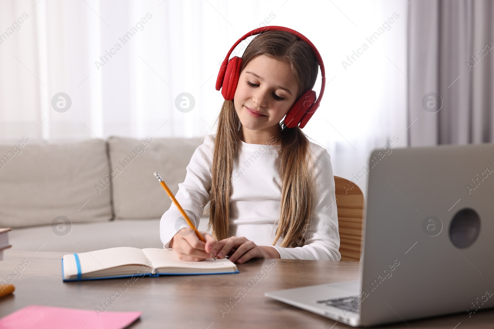 Photo of E-learning. Cute girl taking notes during online lesson at table indoors