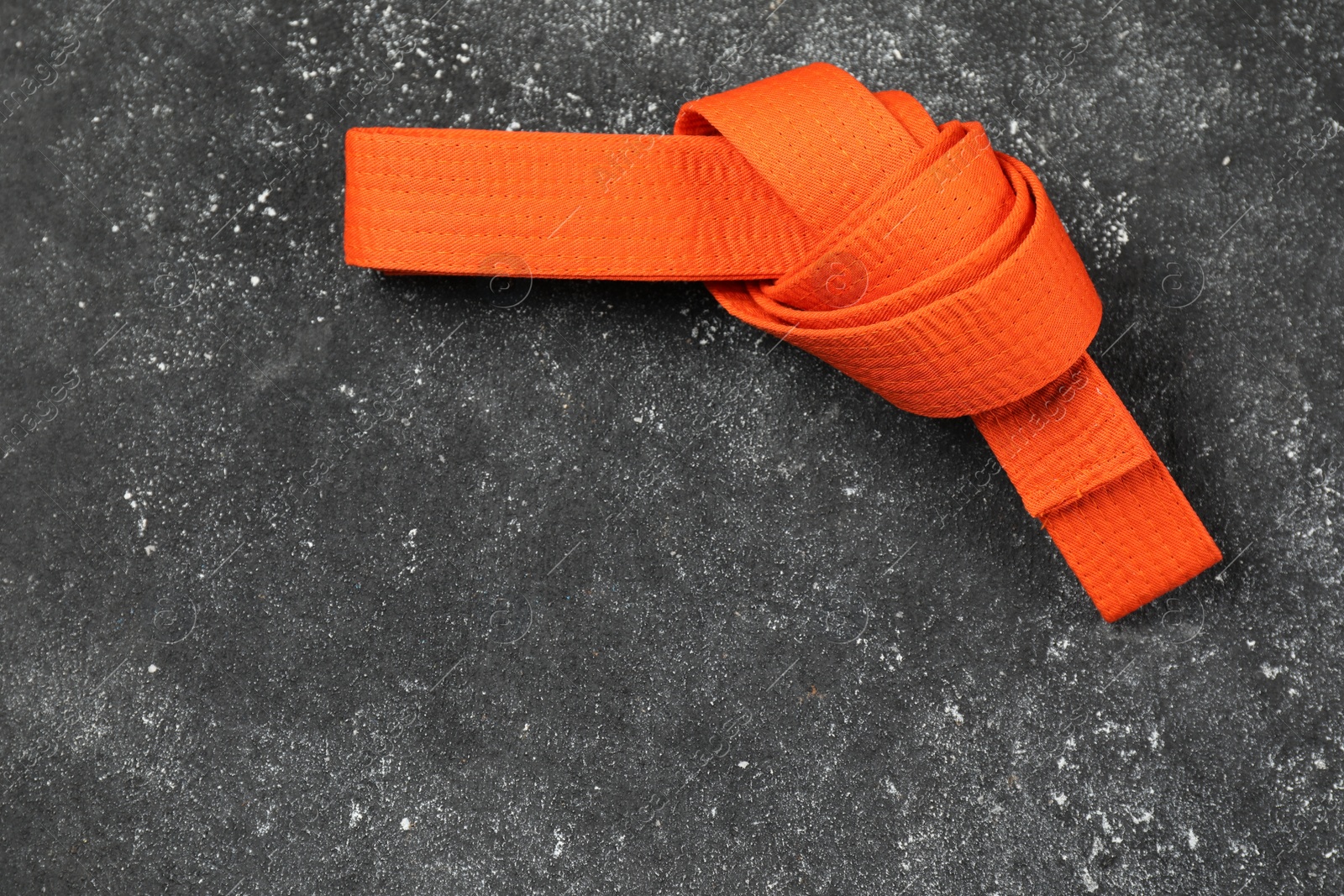 Photo of Orange karate belt on gray textured background, top view. Space for text