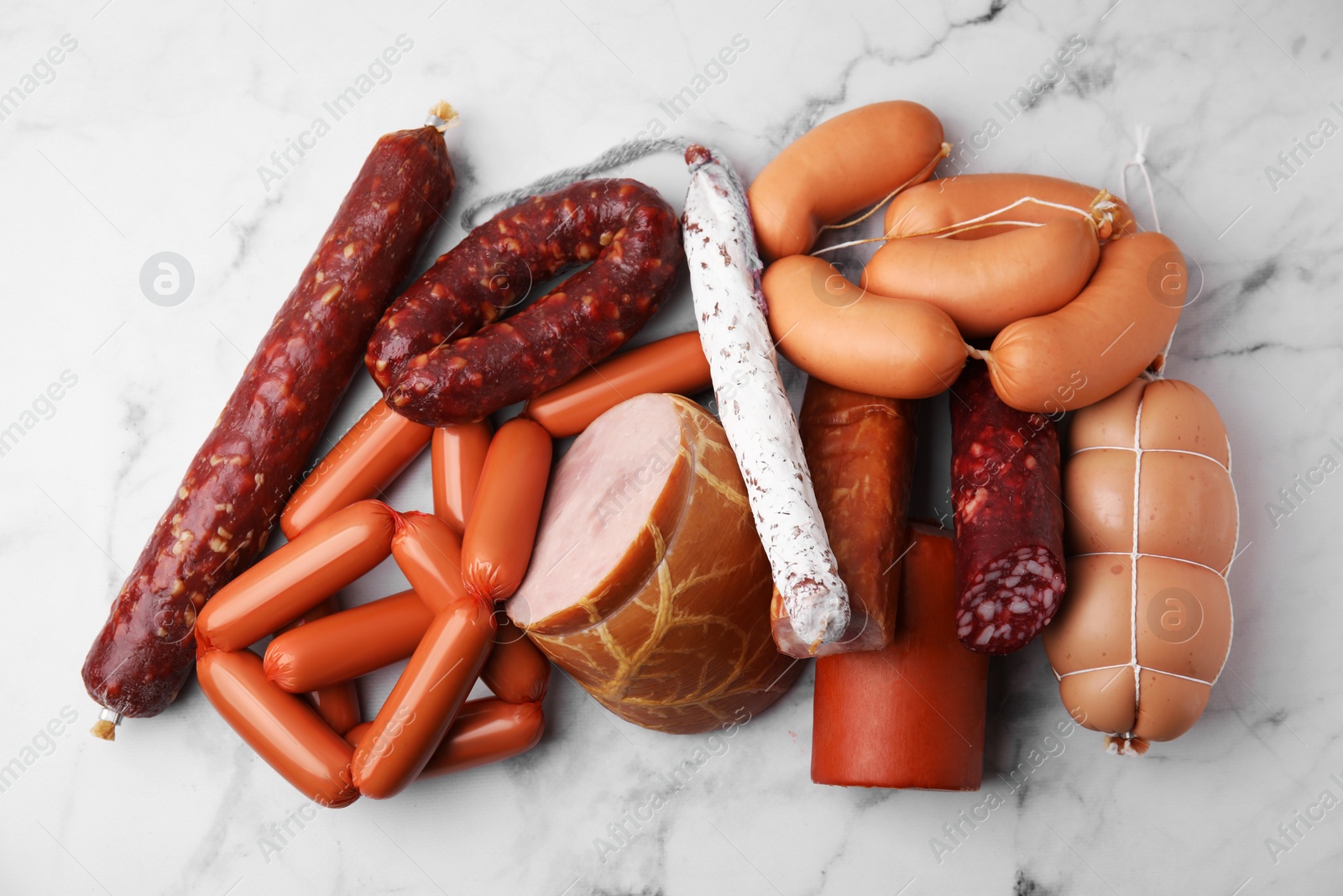 Photo of Different types of sausages on white marble table, flat lay