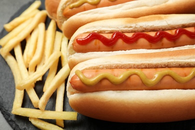 Delicious hot dogs and french fries on slate plate, closeup