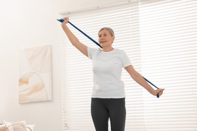 Photo of Senior woman doing exercise with fitness elastic band at home