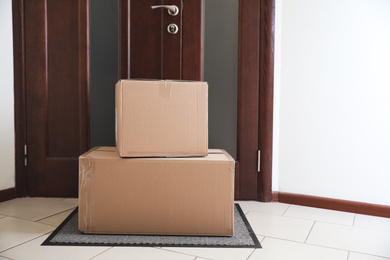 Photo of Cardboard boxes on rug near door. Parcel delivery service