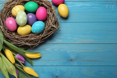 Colorful eggs, nest and tulips on blue wooden background, flat lay with space for text. Happy Easter