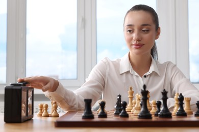 Photo of Woman turning on chess clock during tournament at table indoors