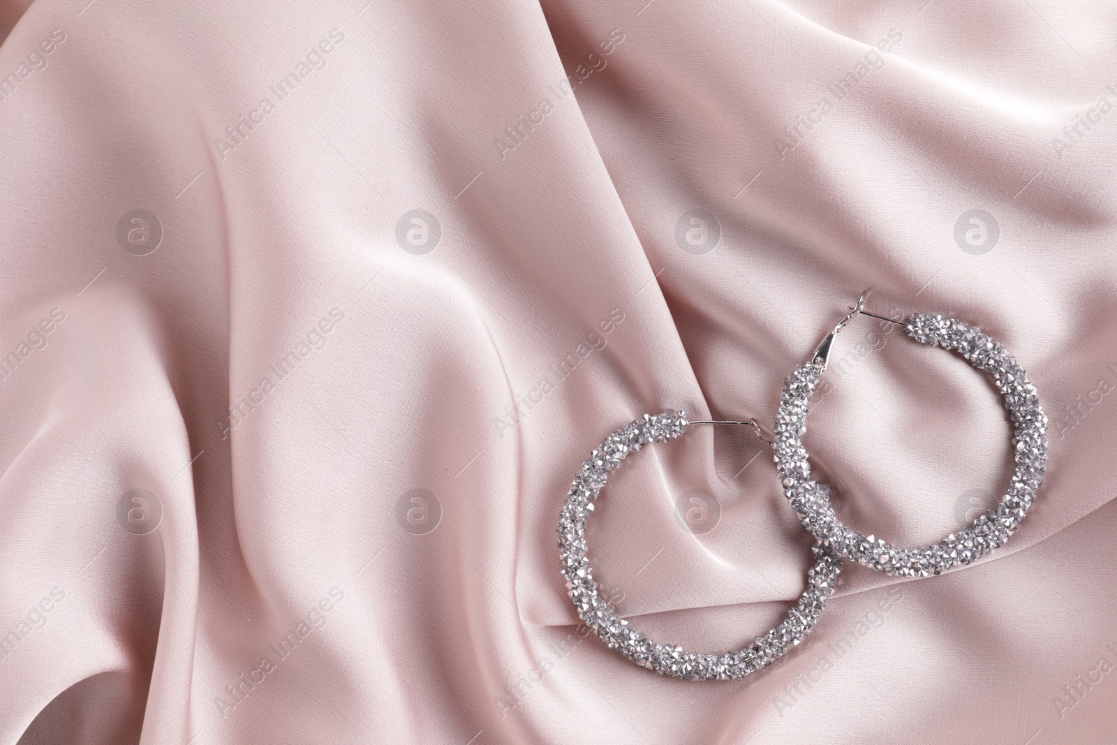 Photo of Elegant jewelry. Luxury earrings on pink silk cloth, flat lay. Space for text