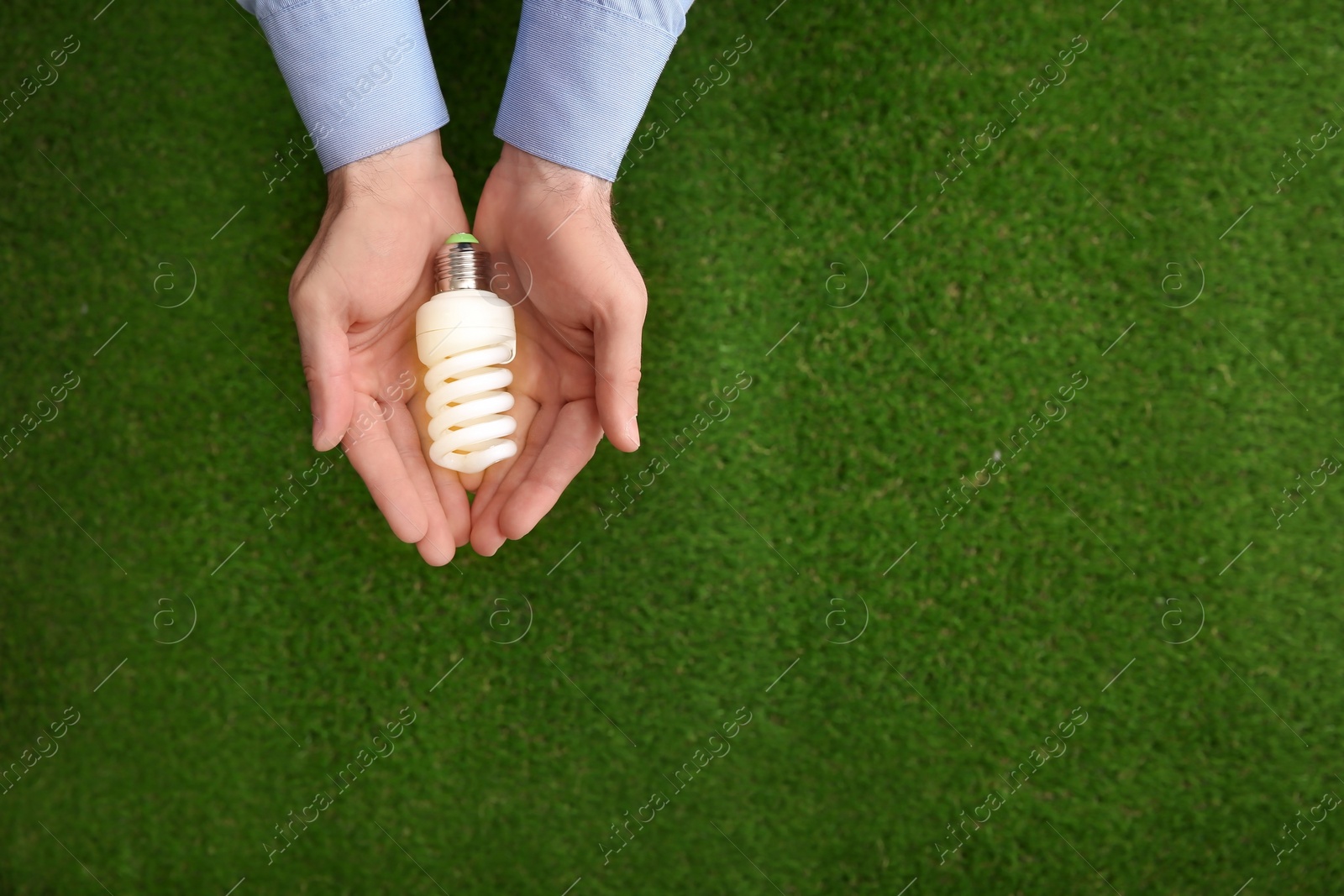 Photo of Man holding energy saving bulb for lamp over green grass, top view. Space for text