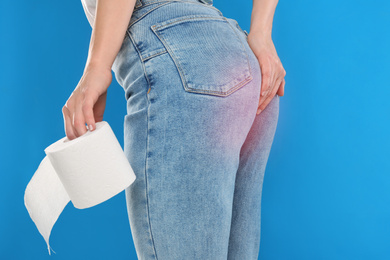 Image of Woman with toilet paper suffering from hemorrhoid on light blue background, closeup