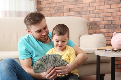 Photo of Happy father and son with money at home