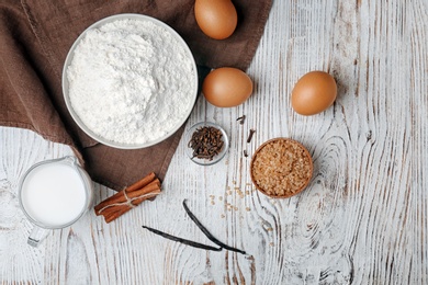 Photo of Bowl with flour, eggs and jug of milk on wooden background, top view