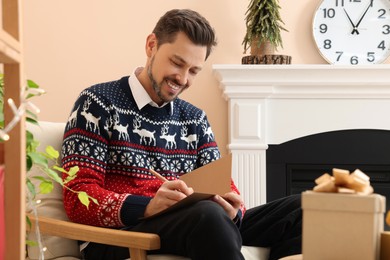 Happy man writing wishes in Christmas greeting card in living room