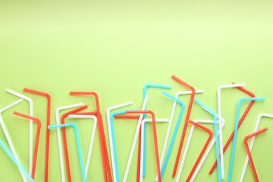 Photo of Colorful plastic drinking straws on green background, flat lay. Space for text