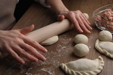 Photo of Woman rolling dough for chebureki on wooden table, closeup