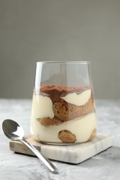 Delicious tiramisu in glass and spoon on grey textured table, closeup