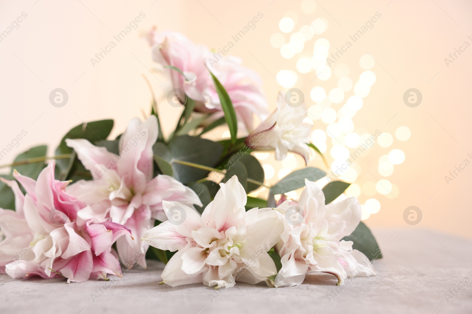 Photo of Bouquet of beautiful lily flowers on table against beige background with blurred lights, closeup