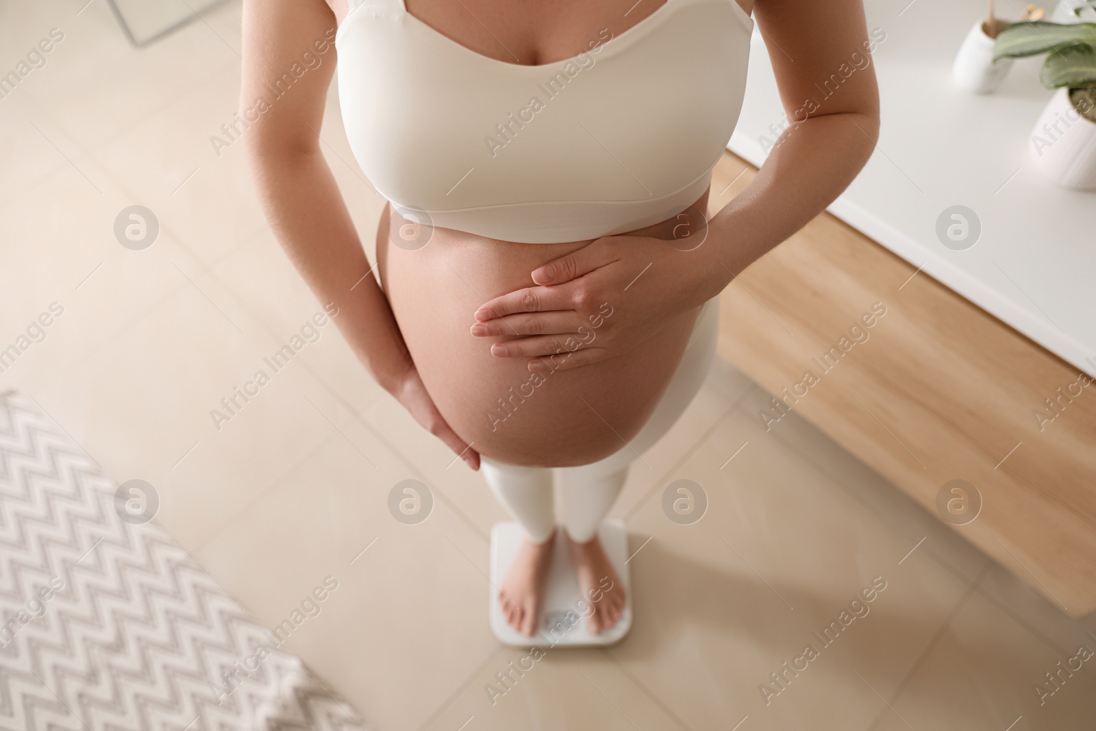 Photo of Pregnant woman standing on scales at home, above view