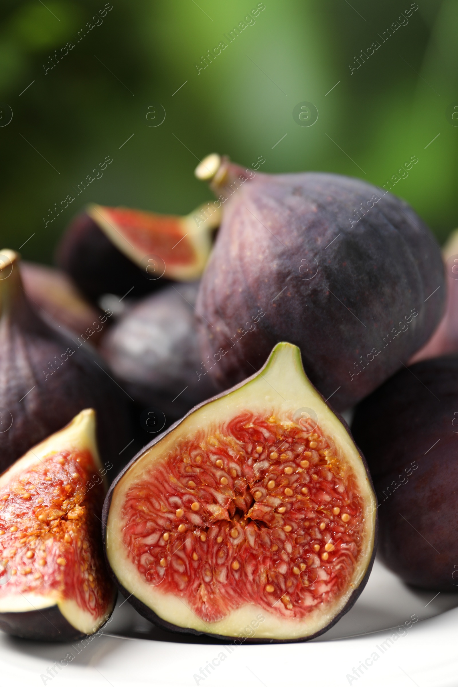 Photo of Whole and cut ripe figs on plate against blurred green background, closeup