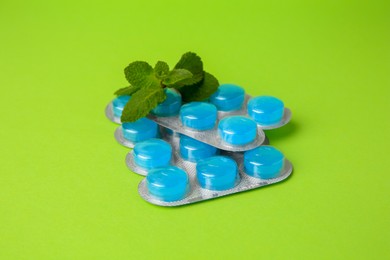 Blisters with cough drops and mint leaves on light green background