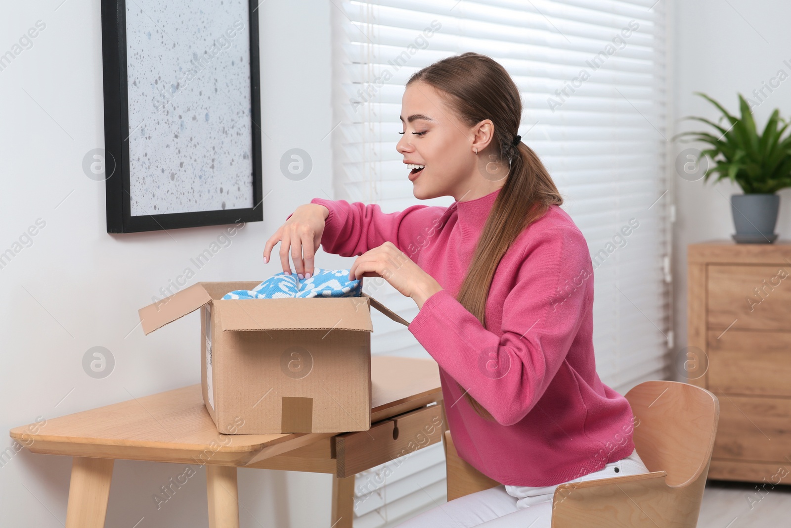 Photo of Emotional woman unpacking parcel at home. Online store