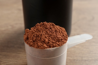 Scoop of chocolate protein powder on wooden table, closeup