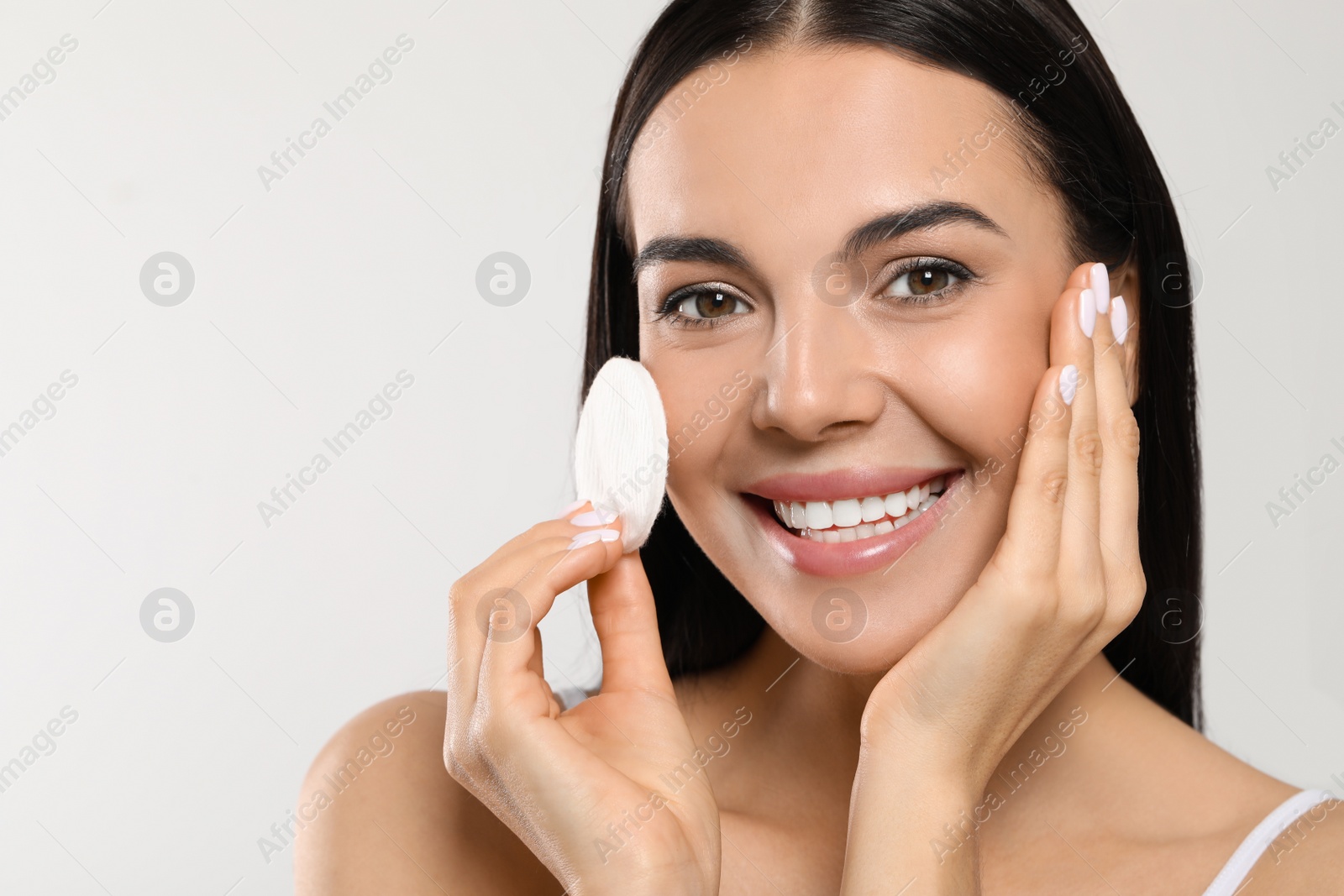 Photo of Young woman using cotton pad with micellar water on light grey background