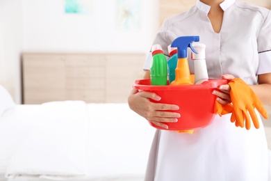 Young chambermaid with cleaning supplies in hotel room, closeup. Space for text