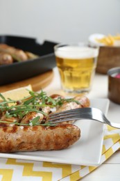 Photo of Tasty grilled sausages served with arugula and beer on white wooden table, closeup