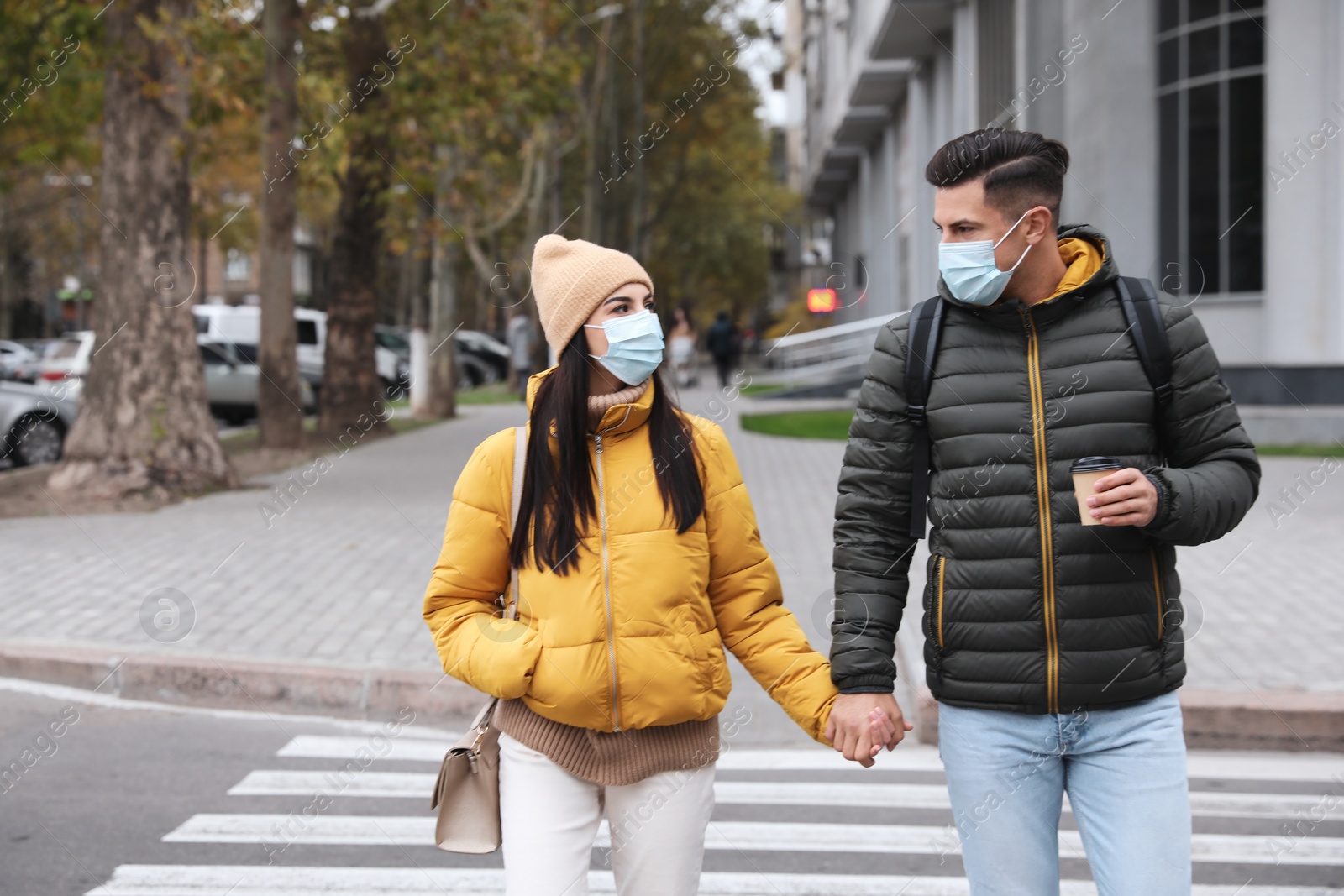 Photo of Couple in medical face masks walking outdoors. Personal protection during COVID-19 pandemic