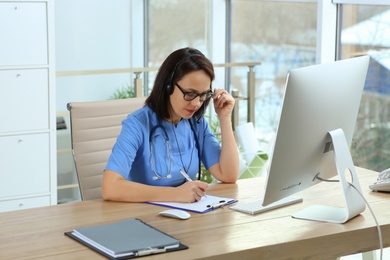 Photo of Doctor with headset and computer consulting patient online in office. Hotline service