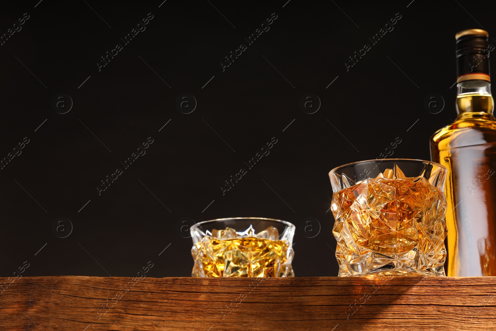 Photo of Whiskey in glasses and bottle on wooden table, low angle view. Space for text