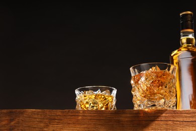 Photo of Whiskey in glasses and bottle on wooden table, low angle view. Space for text