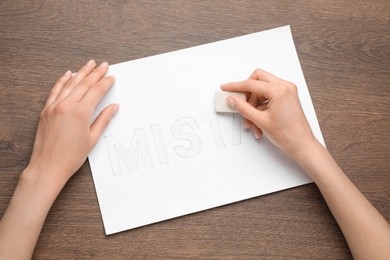 Photo of Woman erasing word on sheet of white paper at wooden table, top view