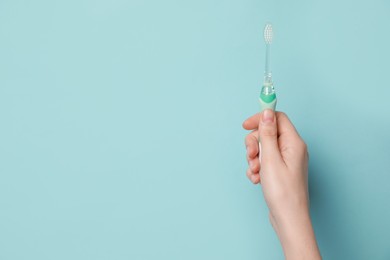 Photo of Woman holding electric toothbrush on light blue background, closeup. Space for text